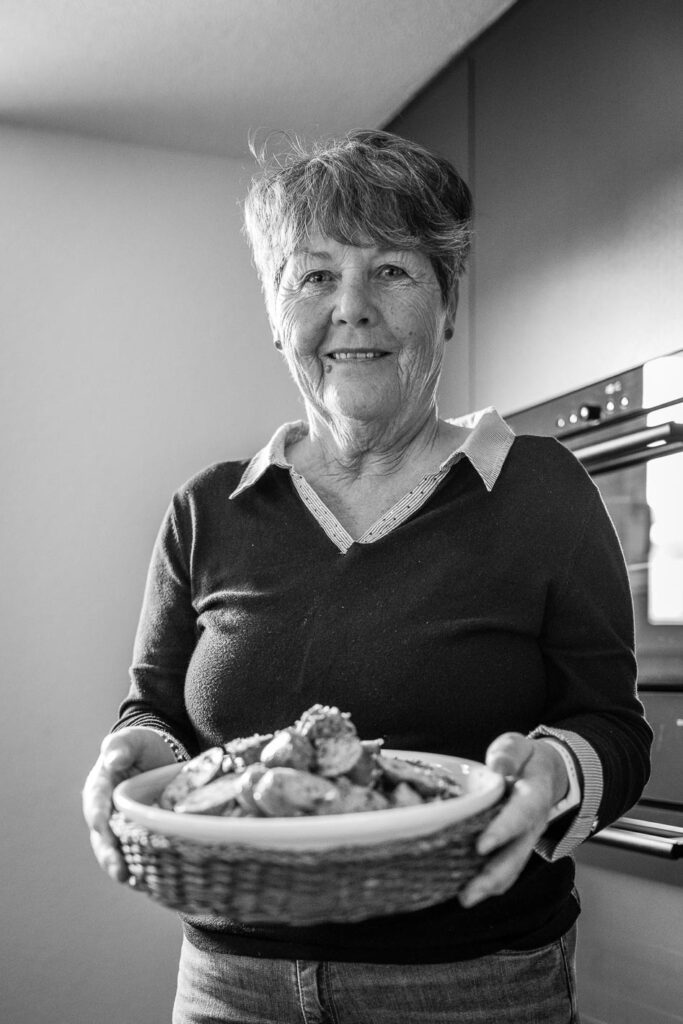 Eine Frau steht in einer Küche und hält eine Platte mit Papet Vaudois vor sich.