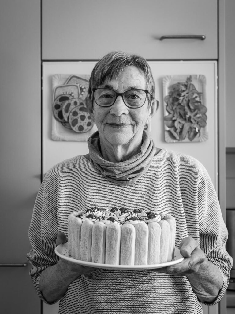 Eine Frau mit Kurzhaarschnitt, Brille und Halstuch hält stolz eine Charlotte Malakoff in den Händen.