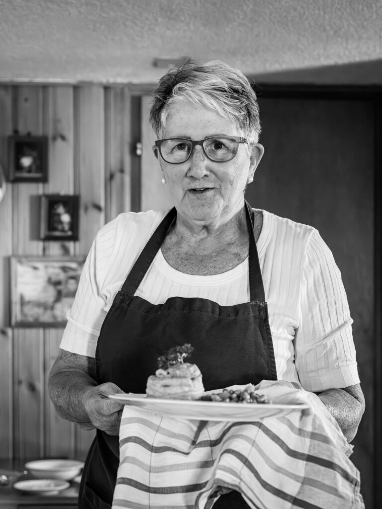 Eine Frau mit Schürze steht in einer mit Holz getäfelten Küche und hält einen heissen Teller mit einem Küchentuch.